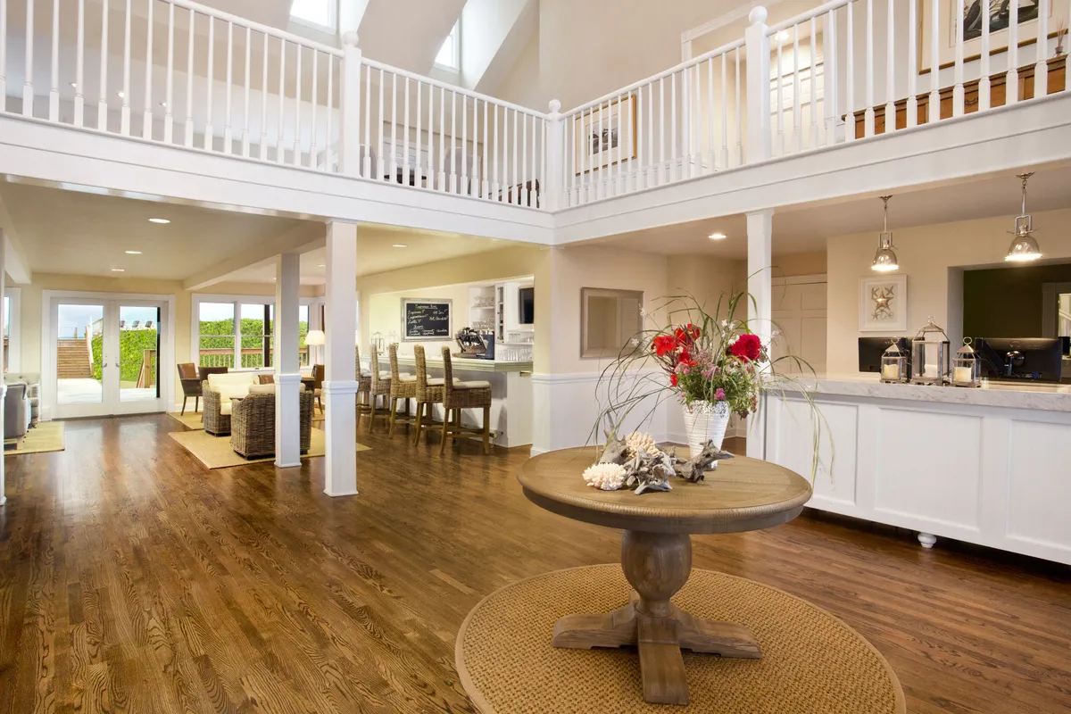 A spacious, open-concept area featuring a central round table with a floral arrangement, seamlessly connecting to a modern kitchen equipped with bar seating. The open flow leads toward an outdoor area, emphasizing the space's suitability for family meals, entertaining, and shared culinary experiences.
