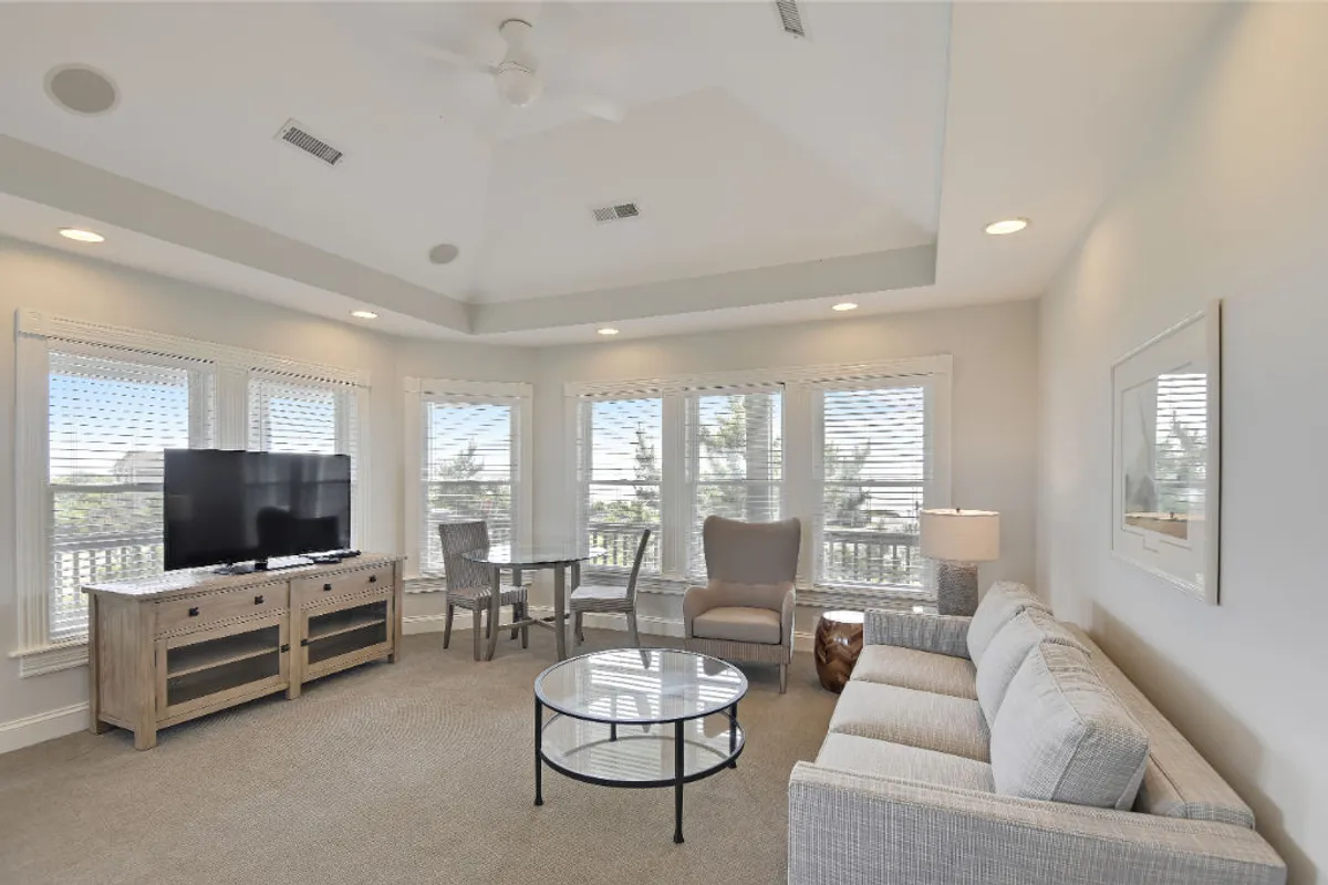 A sun-drenched living area featuring a plush sofa, a coffee table perfect for games or snacks, a large television for movie nights, and windows offering scenic views of nature. The space feels comfortable and serene, inviting guests of all ages to relax and unwind.