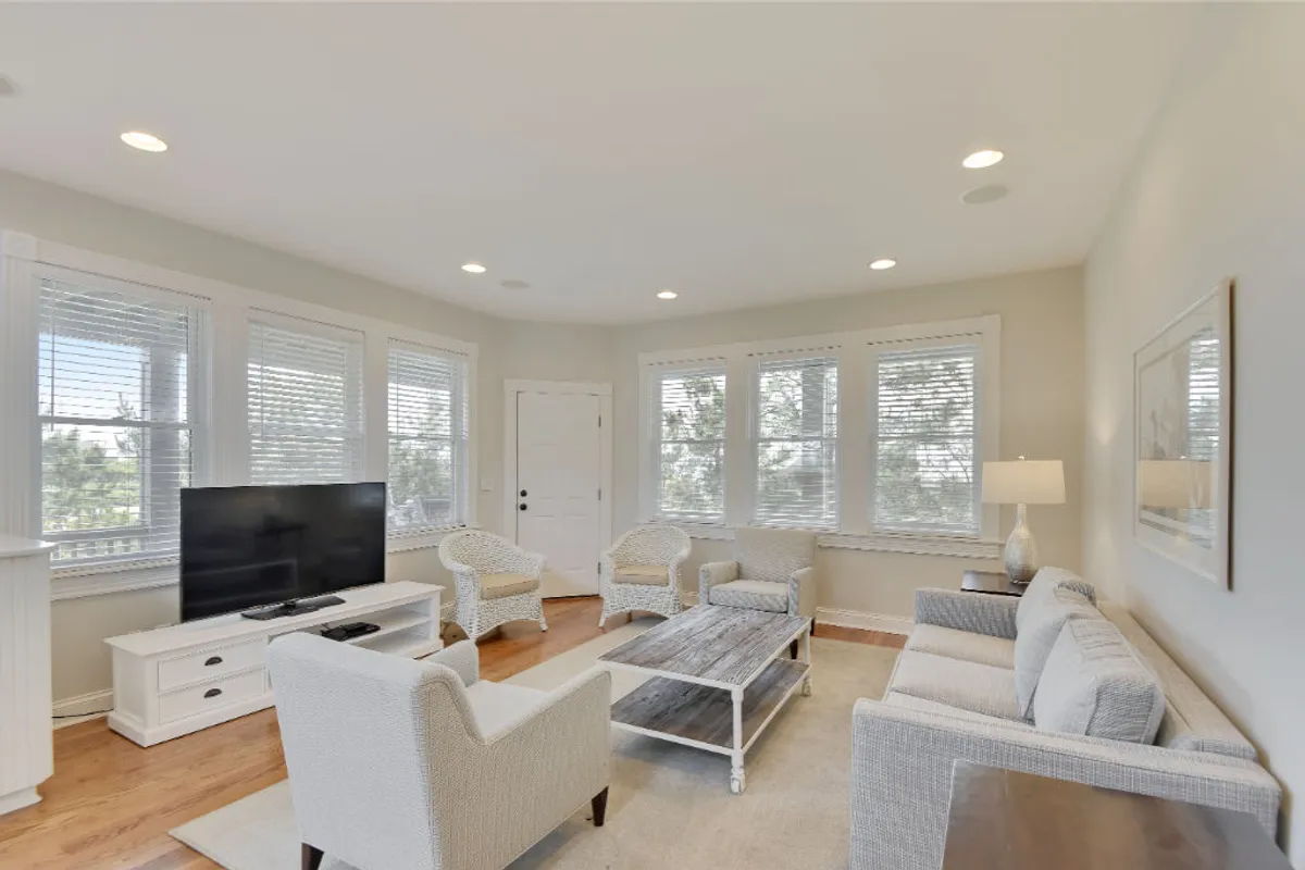 A cozy, inviting living room setting with a comfortable sofa set arranged for both intimate conversations and group gatherings. The coffee table and television make it an ideal spot for family movie nights or casual lounging. Natural light streams in through the windows, enhancing the welcoming atmosphere.
