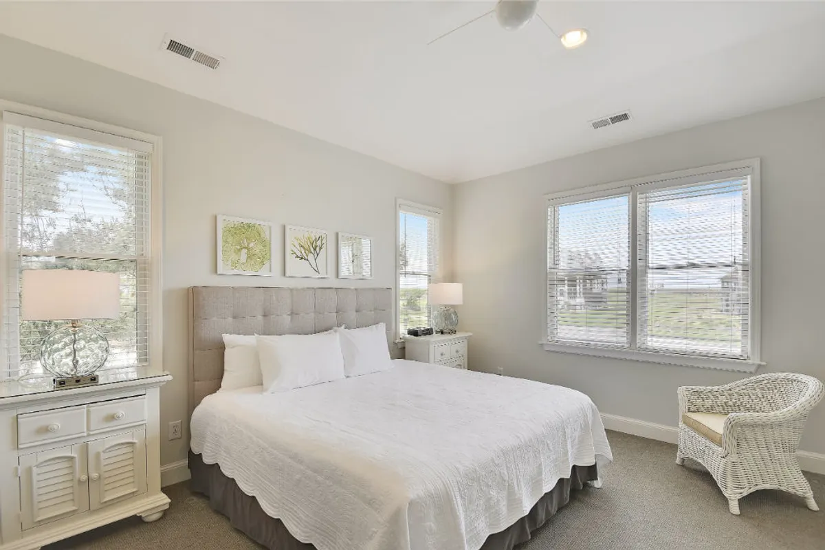 A tranquil bedroom setting with a plush bed, paired side tables, and elegant artwork. A comfortable chair sits by the window, inviting quiet reading or contemplation. Sunlight enhances the peaceful ambiance, ideal for unwinding after a day of adventure.